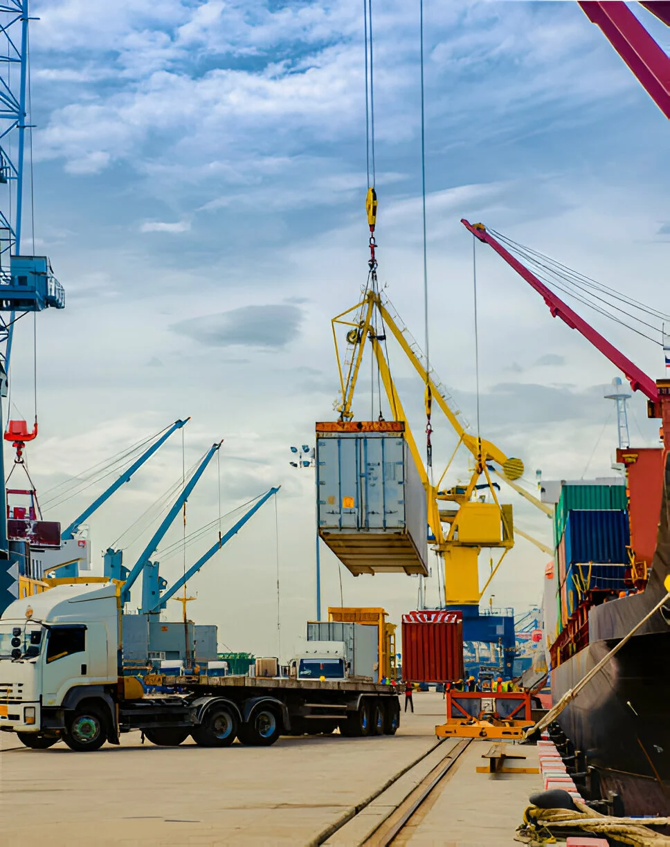 A port crane lifting a container onto a truck beside a docked ship