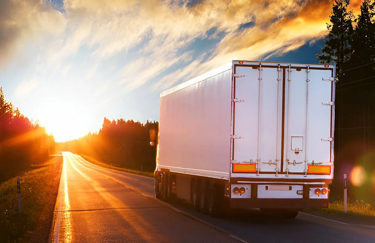 A white freight truck driving into the sunset along an open road